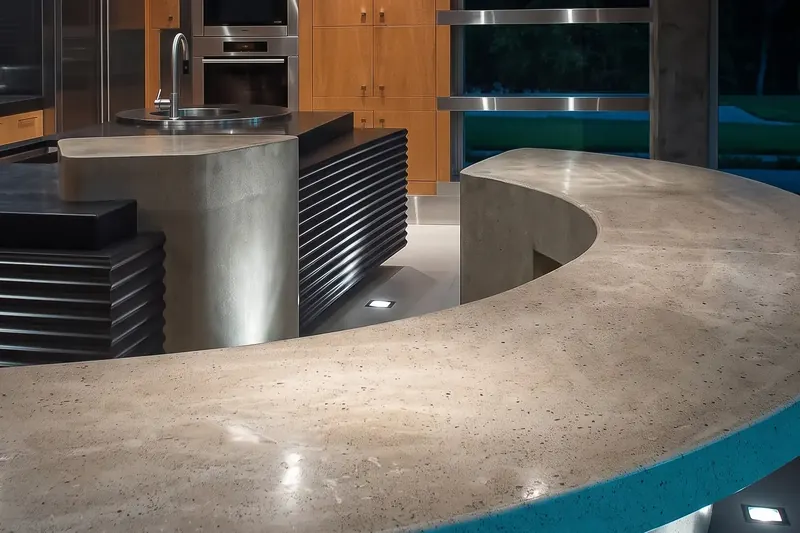 Curved concrete bar top sweeping past a rounded concrete pier and the corrugated black island at dusk