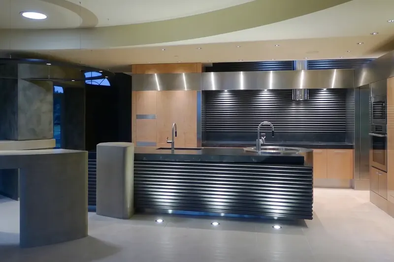 Corrugated black island lit from the floor, set against a ribbed black backsplash under a band of stainless steel