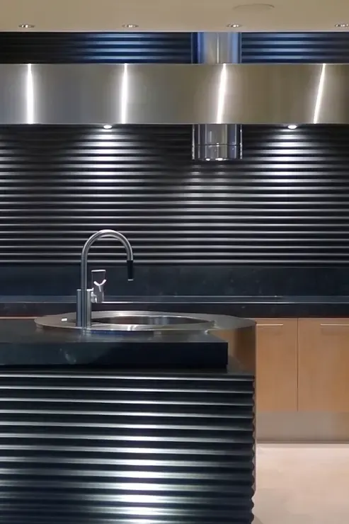 Ribbed black backsplash and tubular vent hood set behind a stainless band, above the island's round sink