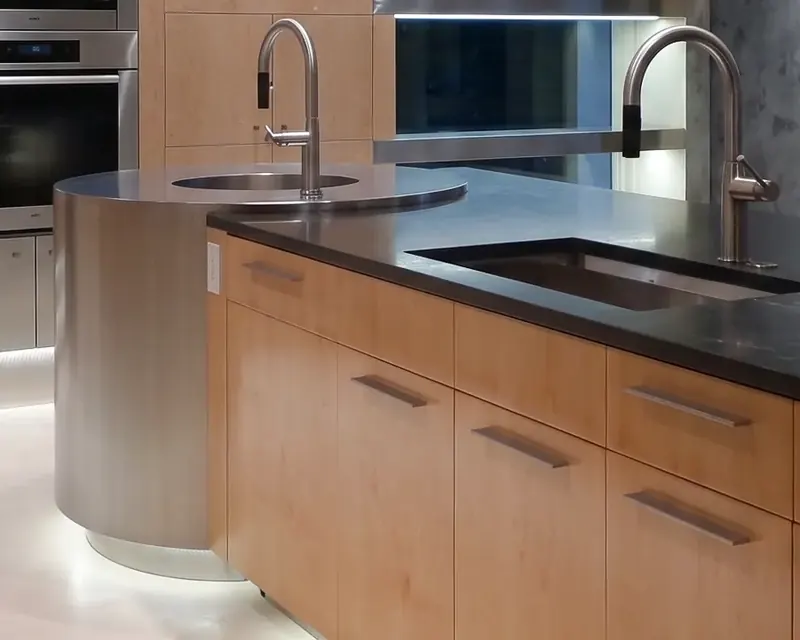 Close view of the round stainless drum sink beside an undermount sink in a dark countertop over maple drawers
