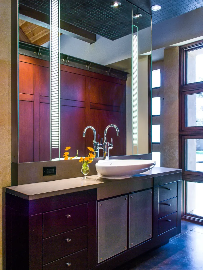 Vanity with a vessel sink, red-stained cabinetry and lit mirror strips