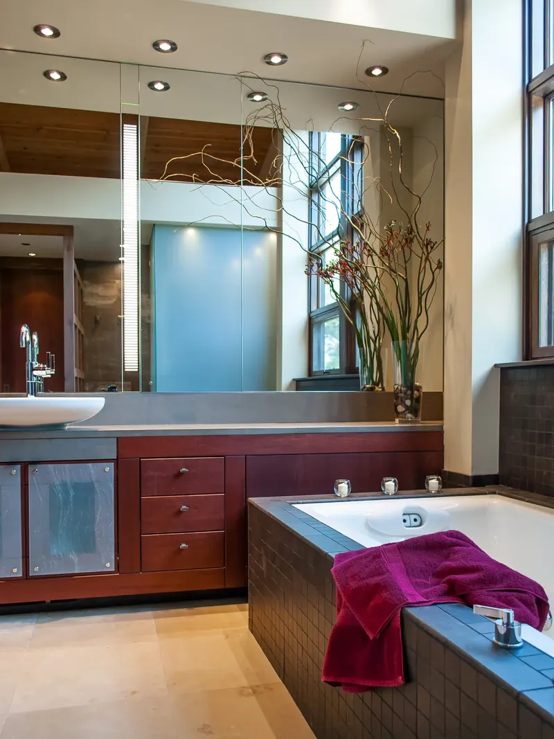 Tiled tub beside a long vanity with red-stained drawers and a mirrored wall