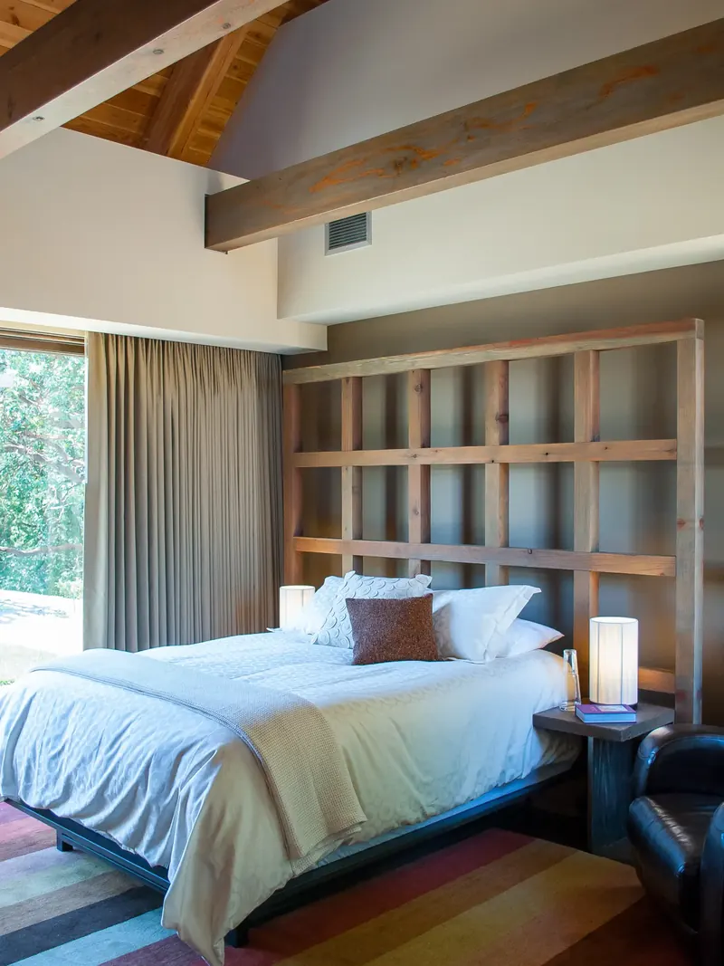 Bed against a timber grid headboard wall, with a leather chair and tall window