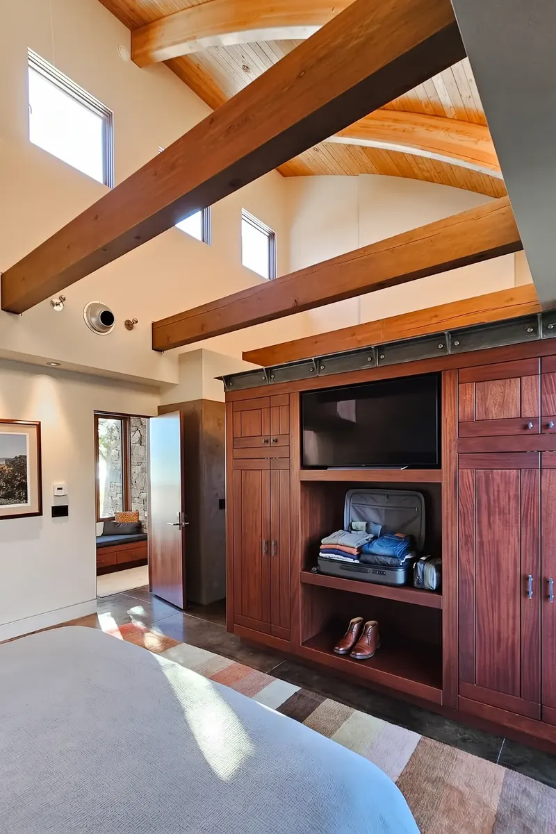 Built-in red-stained cabinet with open shelves beneath curved timber beams