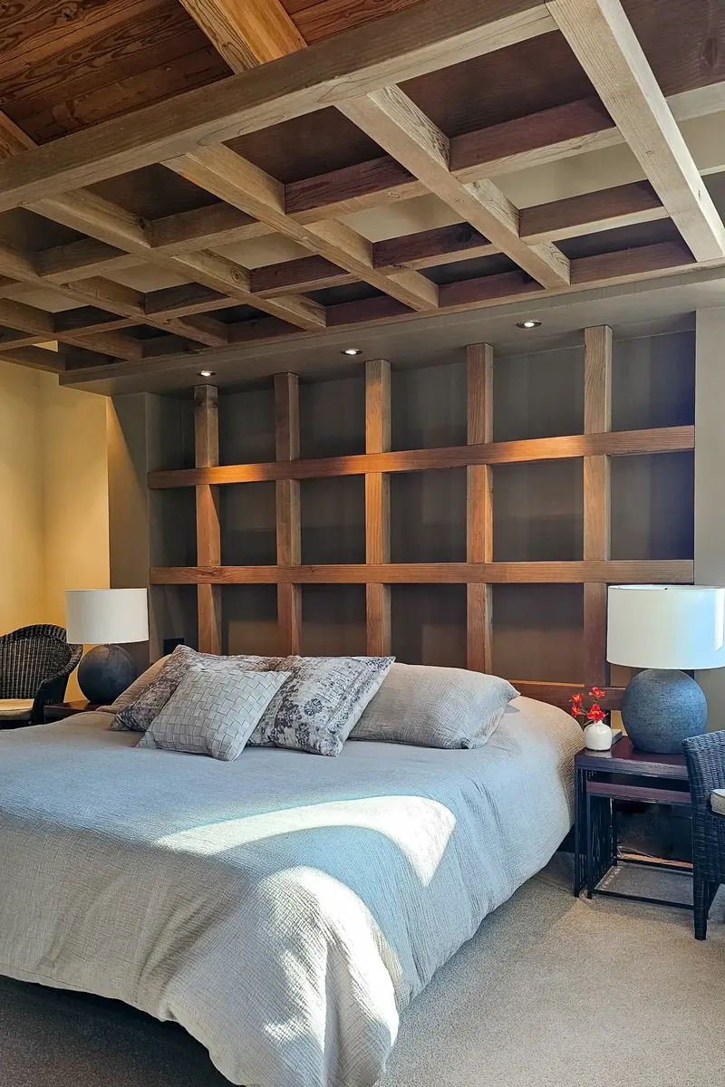 Bedroom with a timber grid wall behind the bed and a coffered wood ceiling