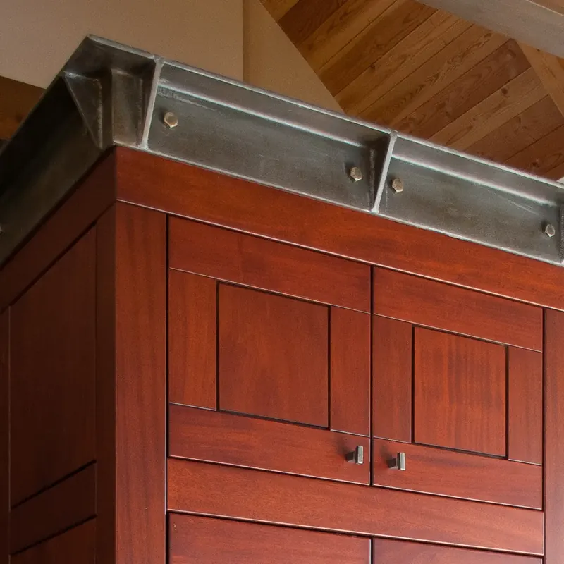 Detail of a red-stained cabinet capped with bolted steel trim