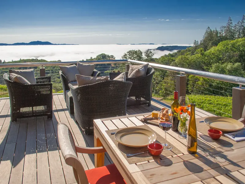 Deck with wicker lounge chairs and a set table overlooking fog filling the valley