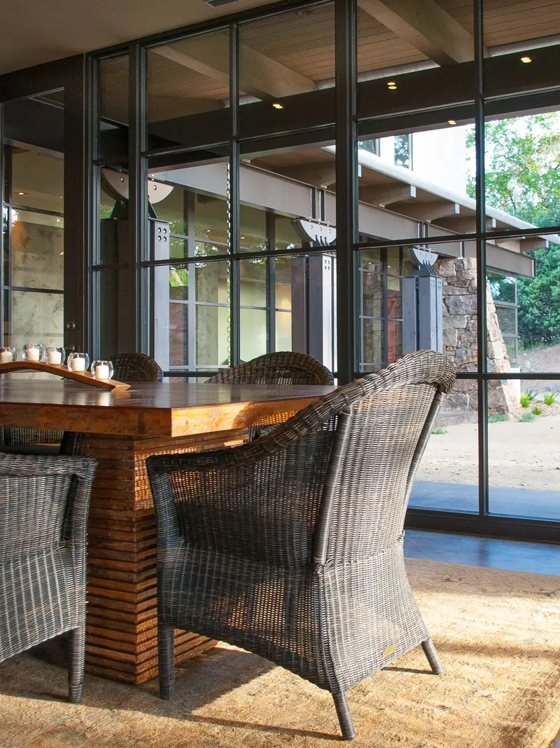 Wicker armchairs at the dining table beside tall windows to the courtyard