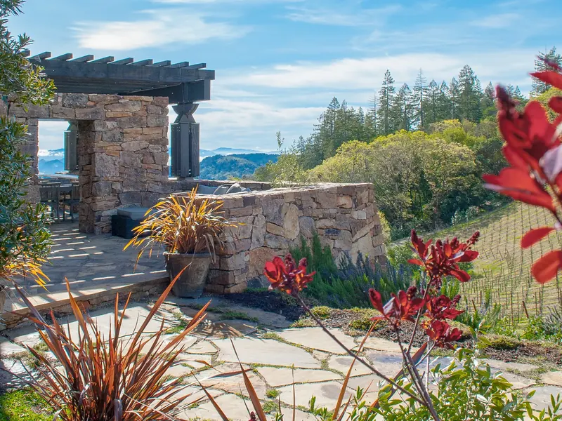 Flagstone courtyard with stone walls and a timber pergola, red flowers in the foreground