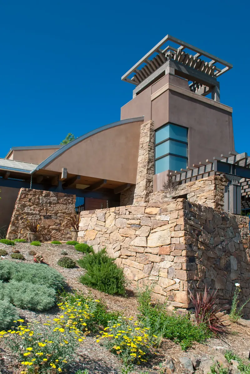 Tower with timber crown and stacked stone walls above a slope of flowering drought-tolerant plants