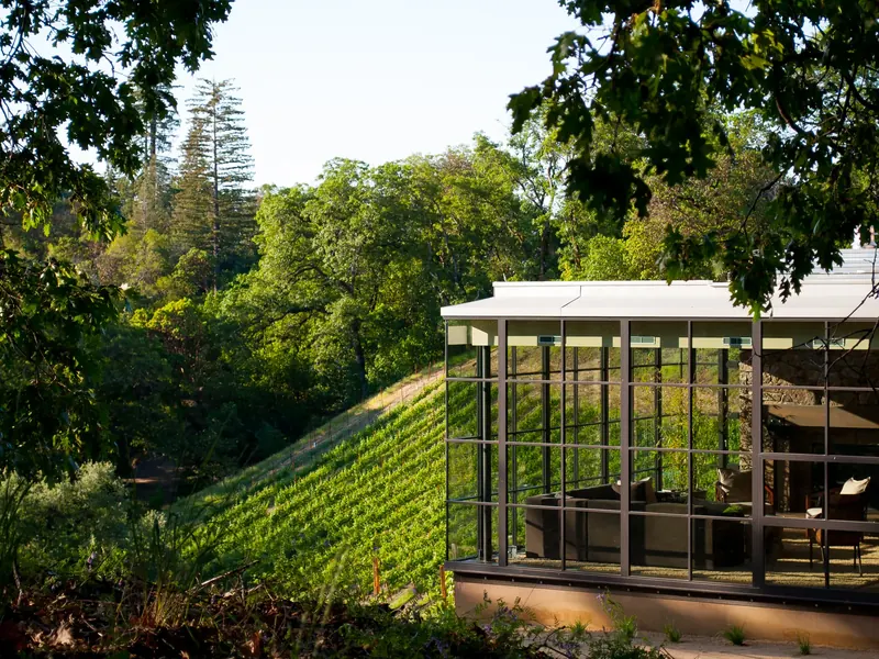 Gridded glass living room seen from outside, set into a hillside of vines and trees