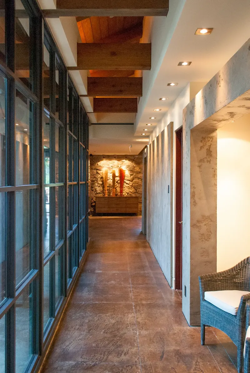 Glass-walled corridor with timber ceiling and a lit stone niche at its end