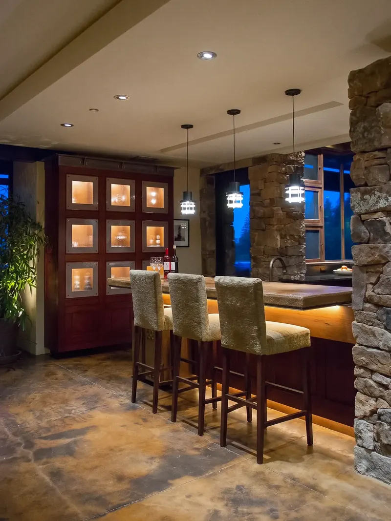 Island bar with upholstered stools, lit display cabinet and a stacked stone column