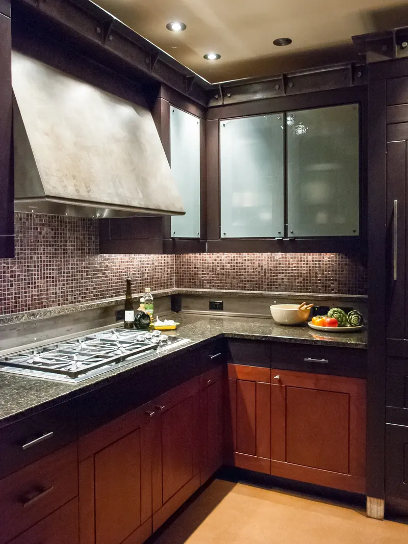 Cooktop corner with a metal hood, mosaic tile backsplash and frosted glass cabinets