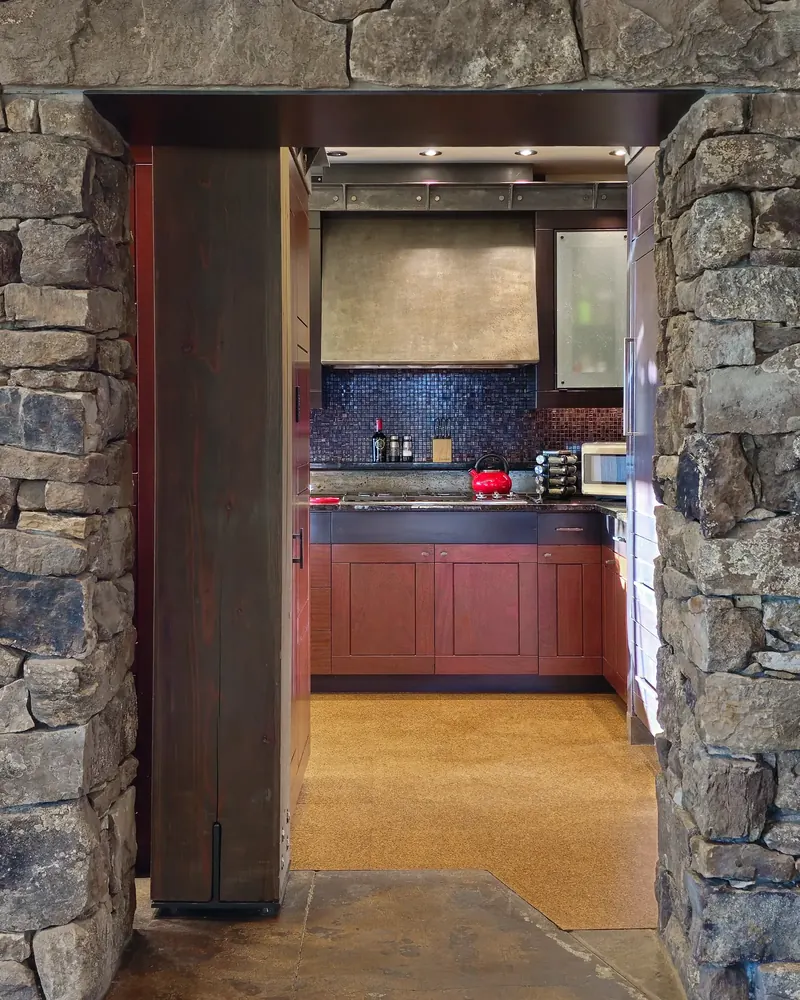 Stone portal with a timber post framing the kitchen and its red-toned cabinetry