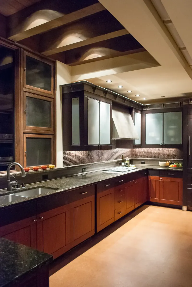 Kitchen with dark stone counters, red-stained cabinets and frosted glass uppers
