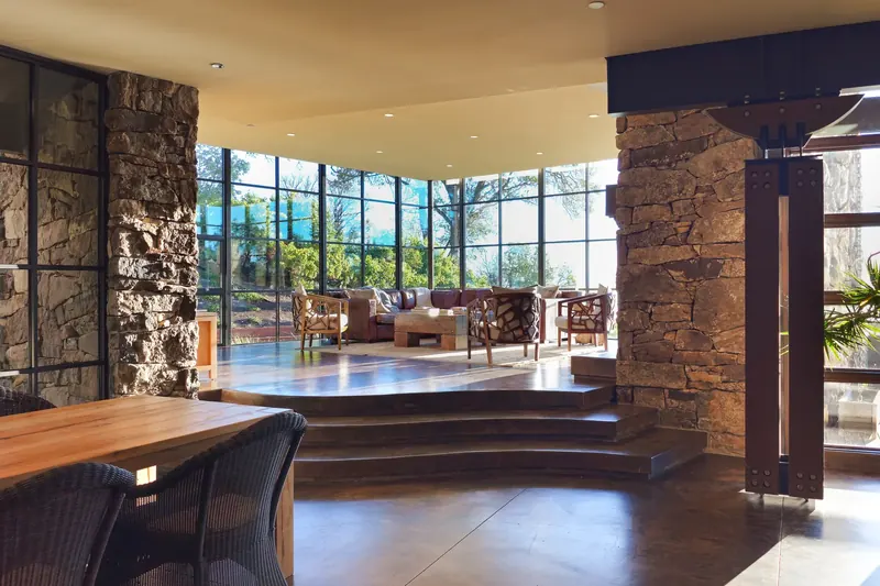 Dining table beside stone piers with steps rising to the windowed living room