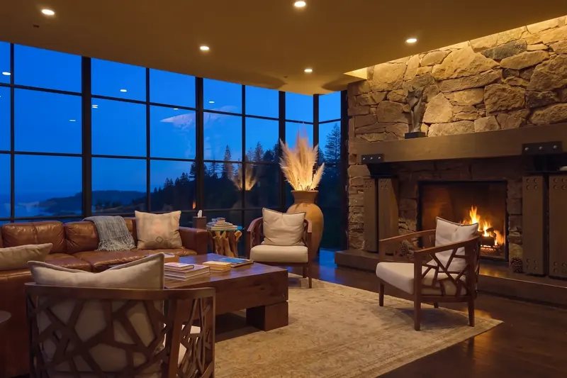 Living room at dusk with a lit fireplace, leather sofa and blue valley view