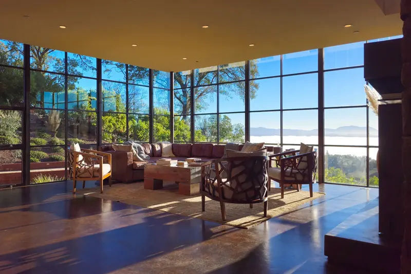 Glass-walled living room at sunrise with low sofas and a view of the fog below