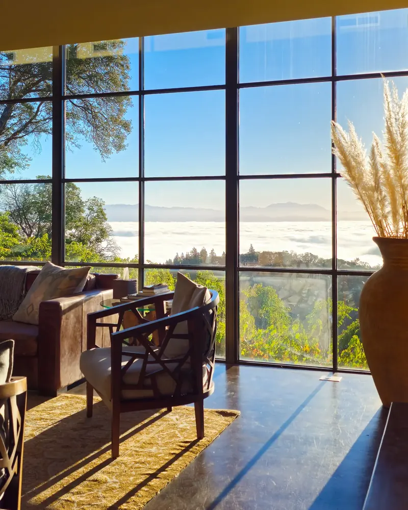 Armchair and sofa by tall gridded windows looking out over fog in the valley