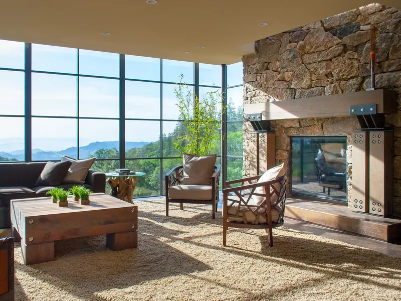 Living room with stone fireplace and floor-to-ceiling steel windows facing the valley