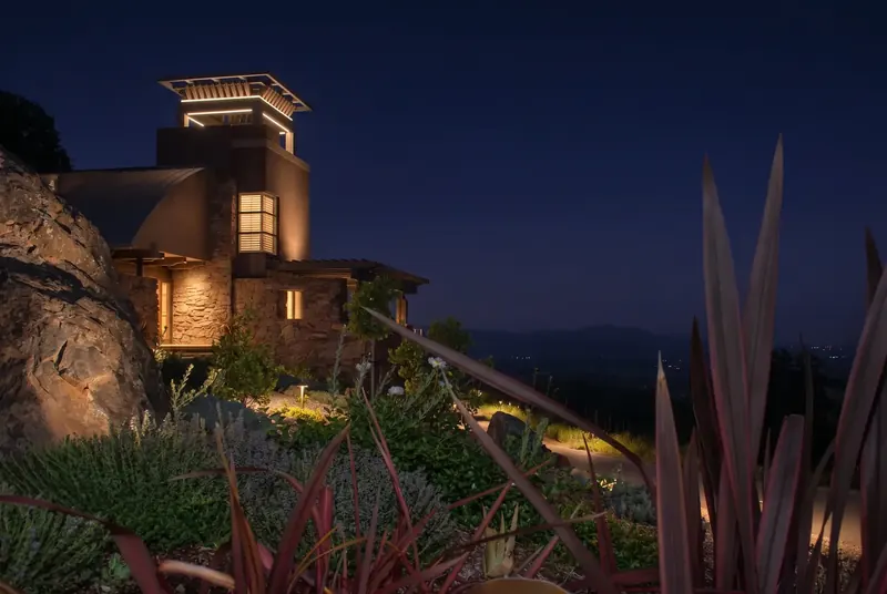 Tower Home on a Vineyard at night, the lit tower beside a rock outcrop and lit garden