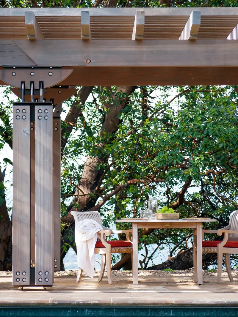 Timber pergola on a steel-banded column above a small table set with a bowl of green apples