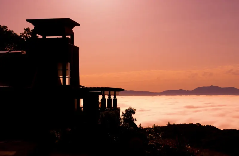 Silhouette of the tower and terrace against a pink dawn sky and fog-covered valley