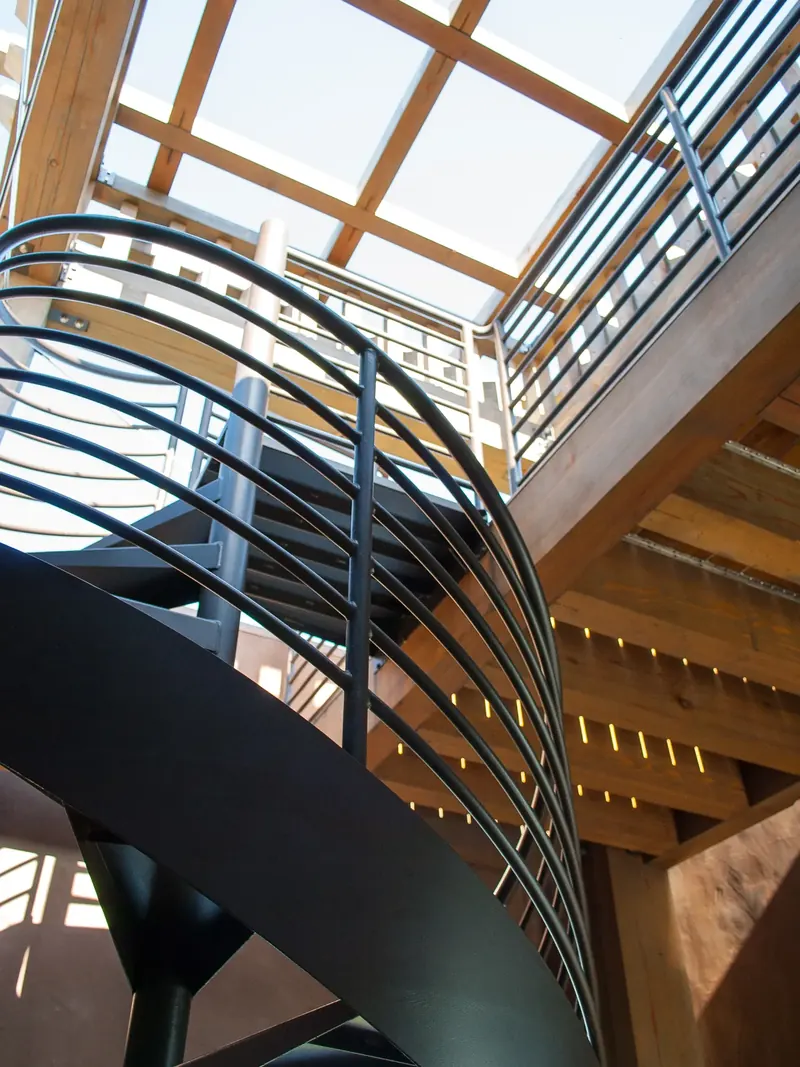Curving steel stair with bent rails spiraling up beneath a timber-framed skylight