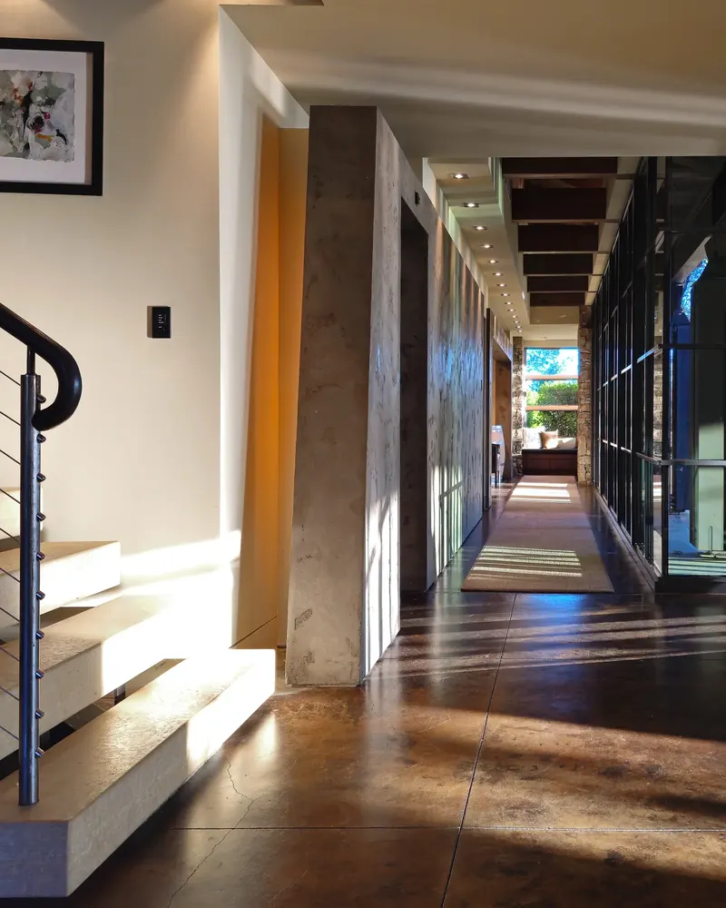 Floating stair beside a long, sunlit corridor with plaster walls