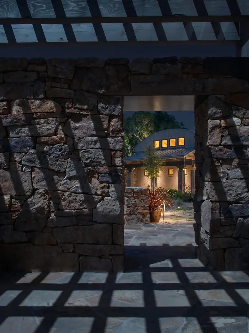 Stone wall opening at night framing the lit courtyard and house beyond