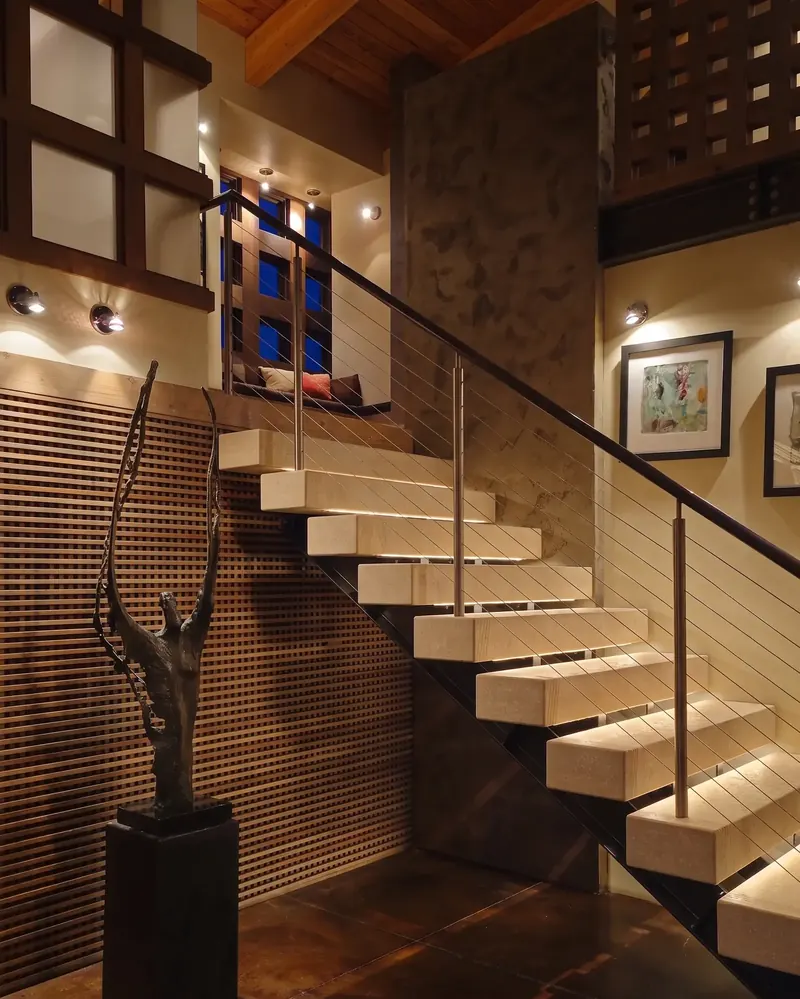 Lit floating stair rising past a bronze sculpture and a textured screen wall