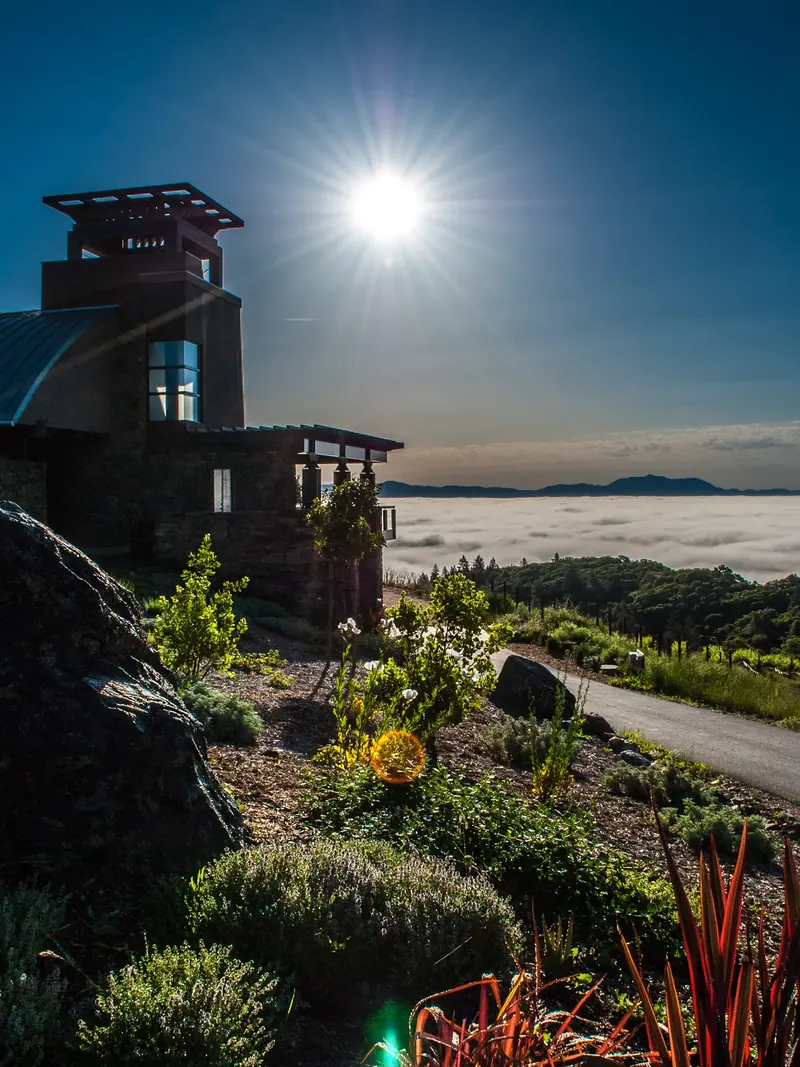 Morning sun over the tower, with a rocky garden slope and fog lying in the valley