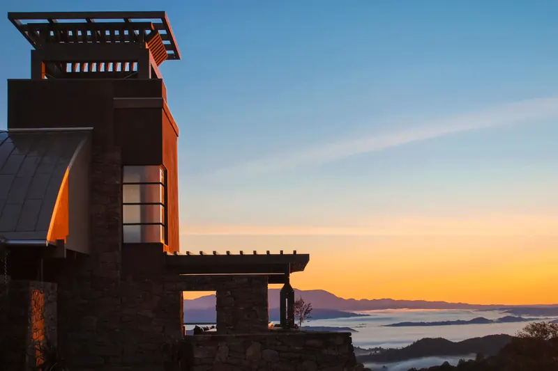 Tower Home on a Vineyard at sunrise, its timber-crowned tower and stone terrace above a fog-filled valley