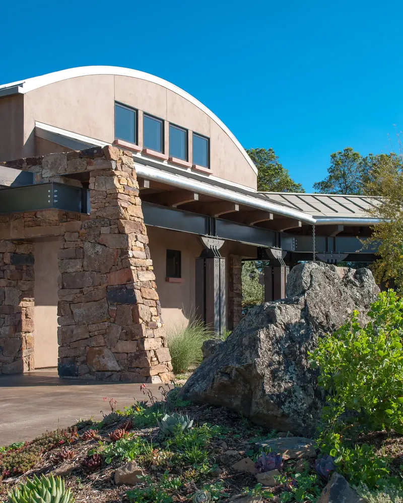 Winery with a curved roof, stone piers and a large boulder in the garden