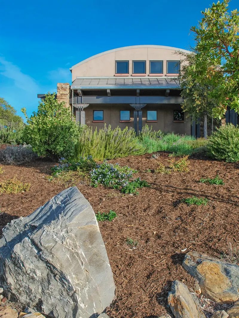 Barrel-roofed winery facade behind a garden of boulders and drought-tolerant plants