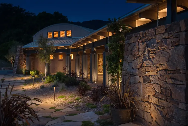 Lit stone wall and covered walkway leading to the winery at night