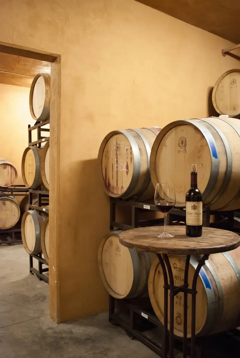 Wine cellar with stacked barrels and a small table holding a bottle and glass