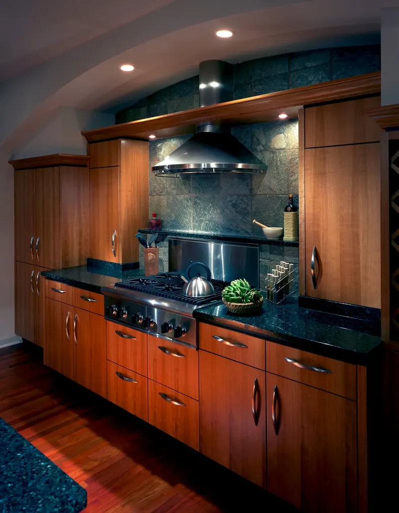 Kitchen with warm wood cabinetry, dark stone counters, stone tile backsplash and stainless hood, Wisconsin