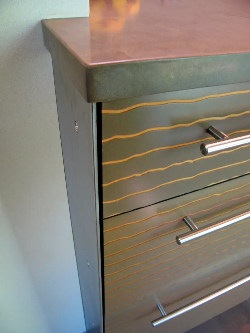 Close detail of drawer fronts with wavy inlaid lines and steel bar pulls beneath a thick countertop