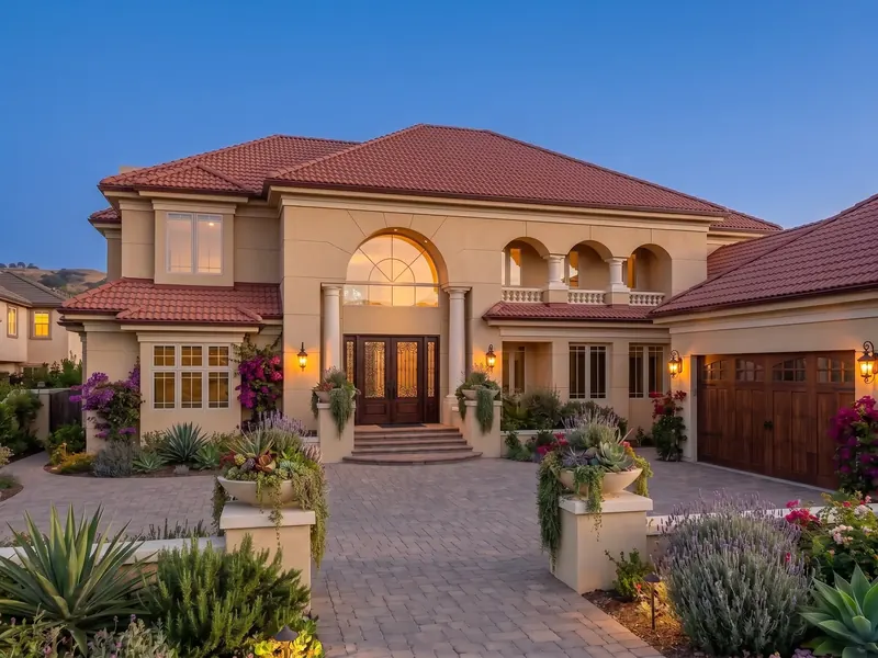 Villa at dusk with arched loggia, lanterns at the entry and a paved motor court with planters