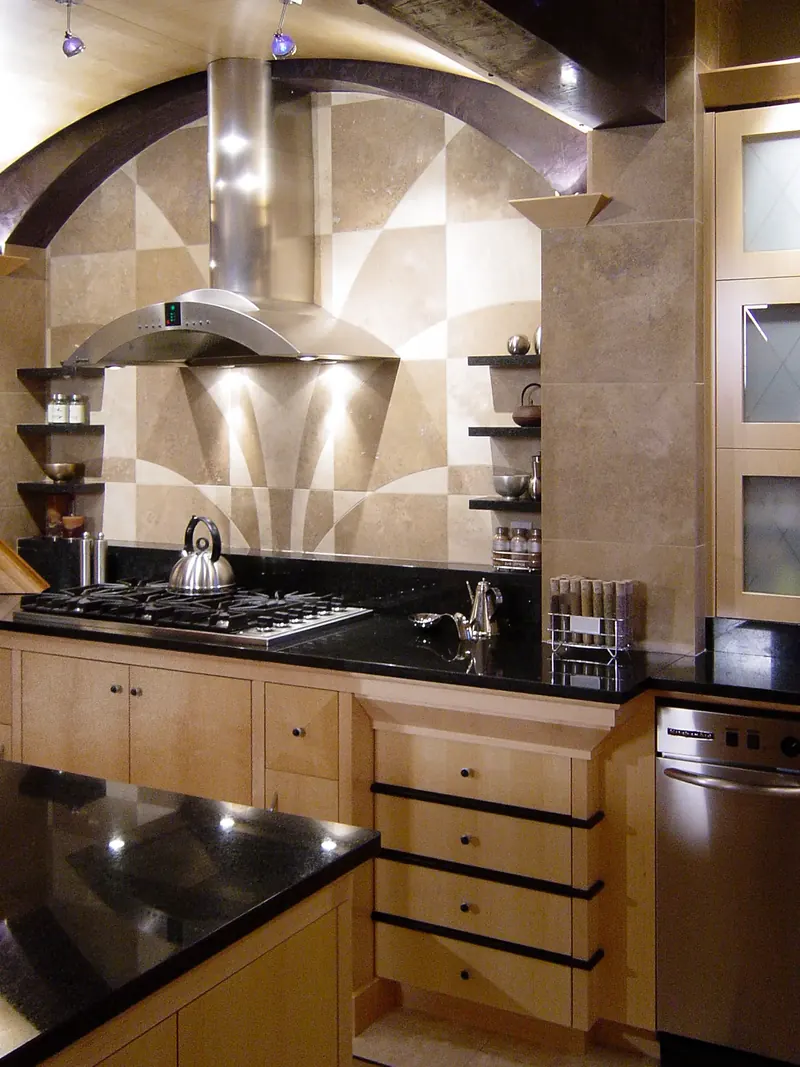 Geometric stone backsplash and stainless hood above a gas cooktop and light wood drawers