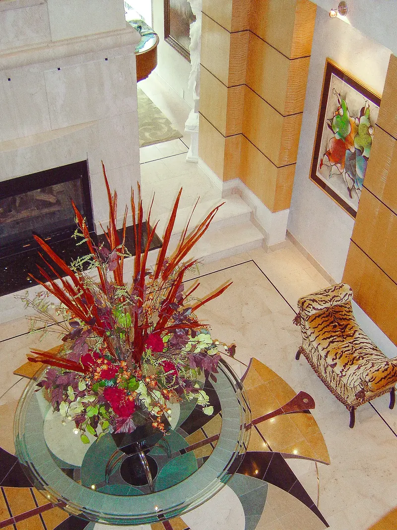 View down onto a glass table with a tall floral arrangement on an inlaid stone floor
