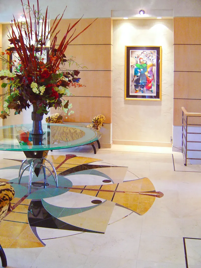 Framed painting in a lit wall niche beyond a glass table with flowers and an inlaid stone floor medallion