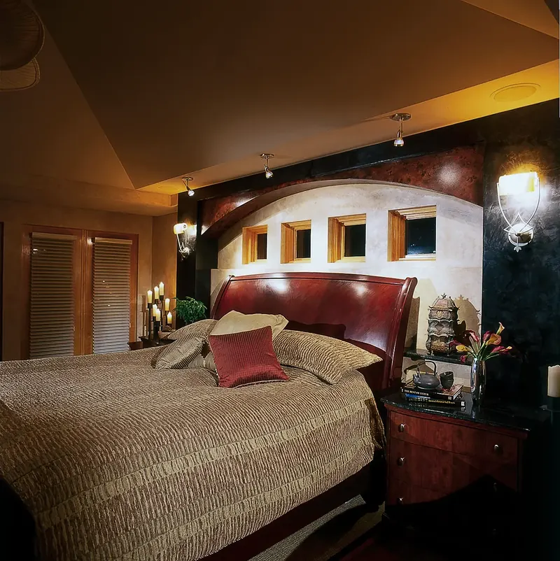 Bedroom with a sleigh bed beneath an arched wall of small square windows, lit by sconces