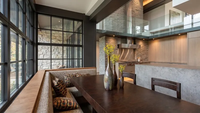 Dining banquette along a steel-framed window wall, open to a kitchen with stone walls, Florida