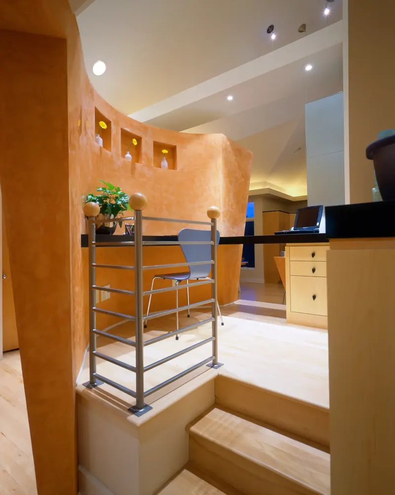 Raised desk nook with a metal rail behind a curved orange plaster wall with small niches