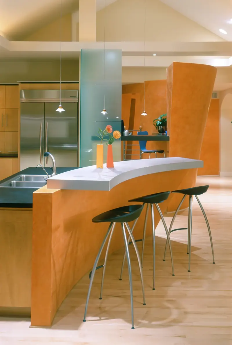 Curved orange island with white top and metal stools beside a frosted glass column