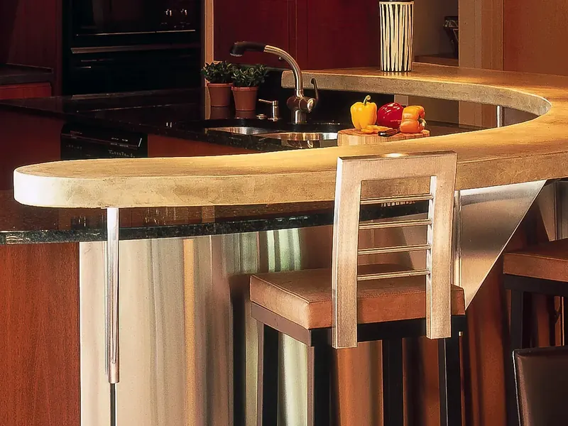 Curved concrete-topped island on a stainless steel base with a bar stool