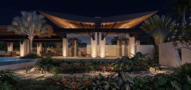Wings in Flight House at night, its wood-lined winged roof glowing above lit concrete columns, glass walls and tropical garden